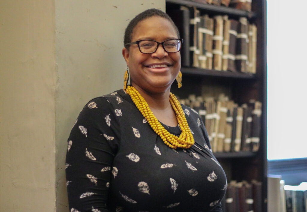 Smiling woman with glasses in a black patterned dress and yellow necklace